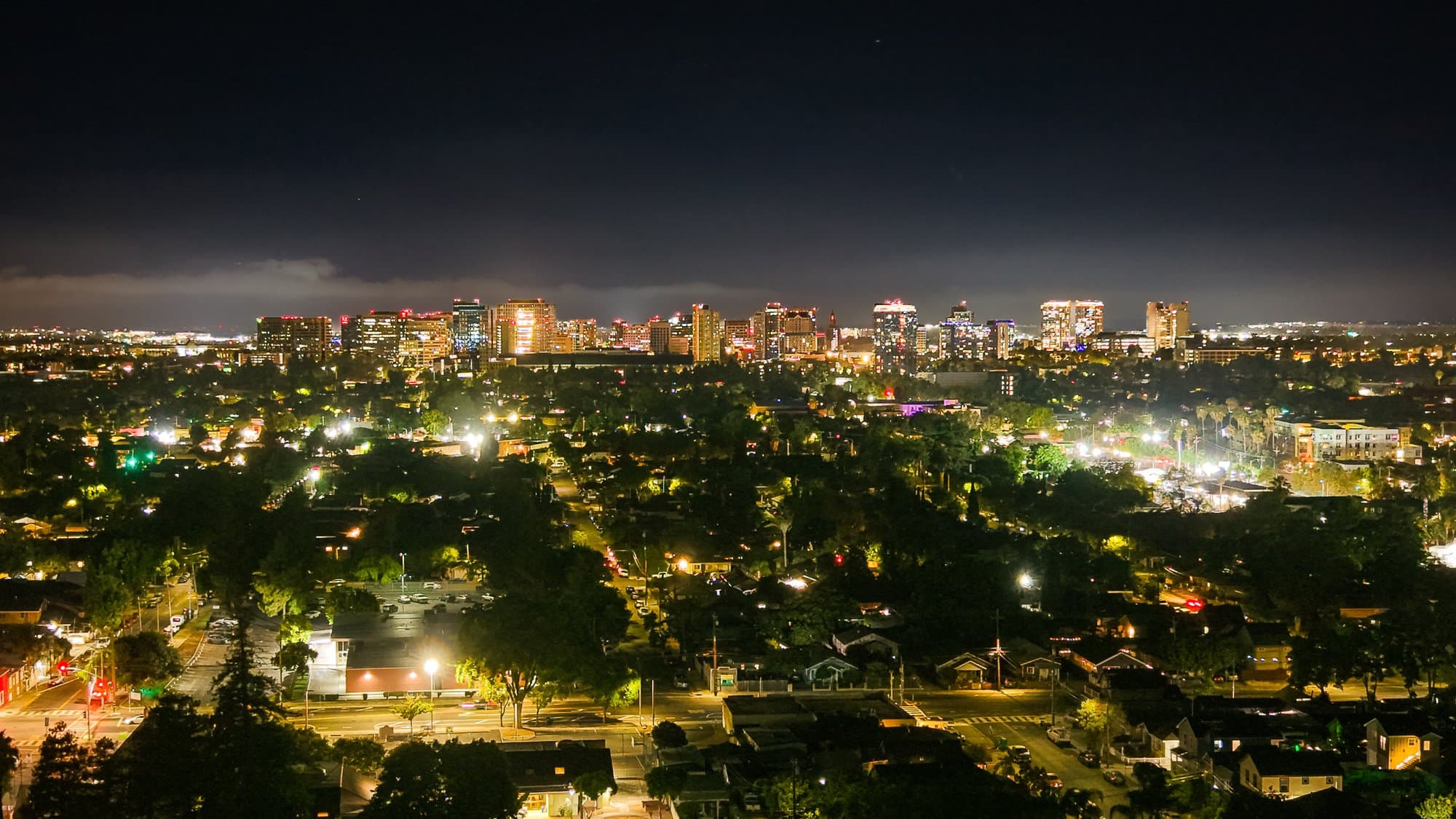 Downtown San José lit up at night, photographed by drone above the surrounding neighbourhoods.
